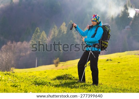 Happy young woman with backpack and trekking sticks hiking in the mountayns against the blue sky with beautiful clouds.