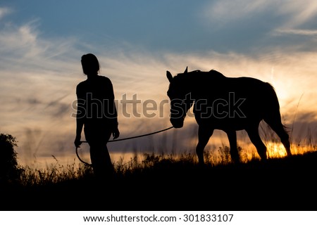 Silhouette of girl leading horse on a leash, sunset in the background