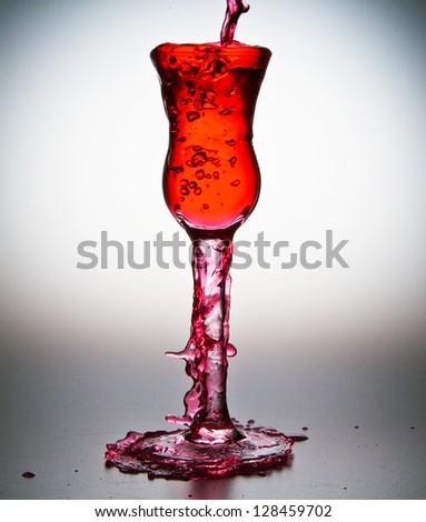 Pink liquid being poured into stemmed cordial glass showing over-spill and splashing of liquid/Overspill
