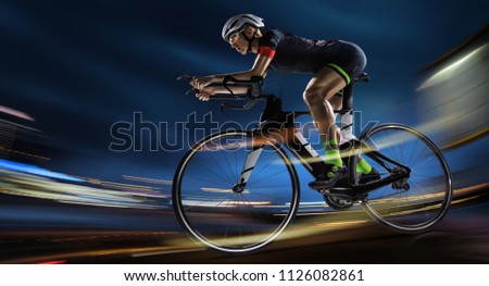 Sport backgrouns. Athletic woman cycling road bike in the evening. Dramatic view of the night city.