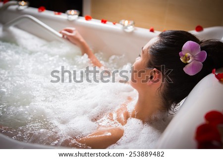 Young woman takes bubble bath with candle.
