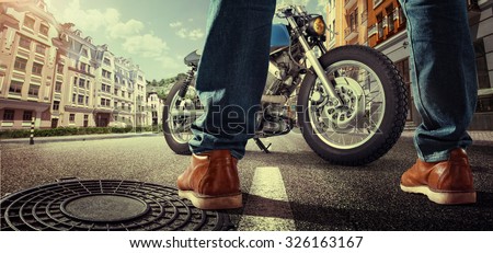 Sport. Biker standing near the motorcycle on the street at sunny day. Close view on legs