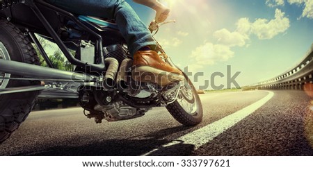 Biker riding on a motorcycle. Bottom view of the legs in leather boots.