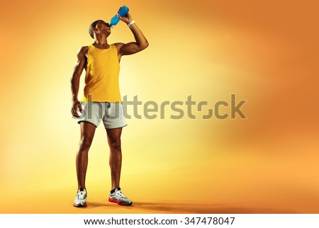 Young muscular build man drinking water of bottle after running, attractive athlete resting after workout outdoors, fitness and healthy lifestyle concept. Isolated on yellow