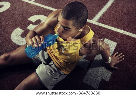 Young muscular build man drinking water of bottle after running, attractive athlete resting after workout outdoors, fitness and healthy lifestyle concept. Start line