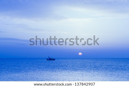 A small fishing boat moves slowly in the Mediterranean Sea under the soft light of the sunset sun.
