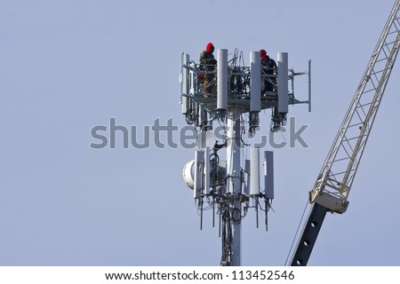 Cellular tower with workers present atop the antennas