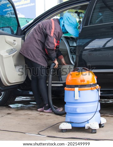 Automobile cleaning theme. Mechanic hoovering the car cabin with vacuum cleaner at auto repair shop garage.