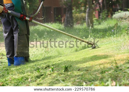 lawn mower worker cutting grass in green field.