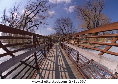 A small bridge crosses a pond with wide angle perspective in Winter