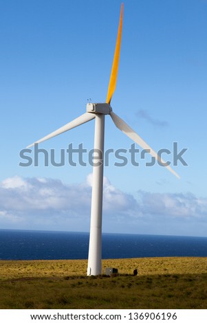 Wind generator spins in an open field overlooking Pacific Ocean