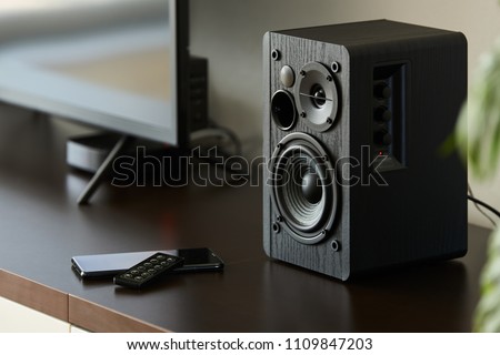 bookshelf speaker with remote controller and smartphone on a TV stand