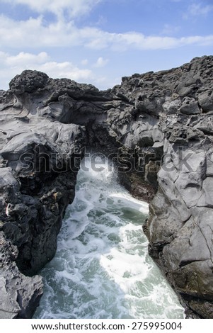 landscape with Spray of water by struck Seawater through tunnel between rocks at the coast near the Olle trail route 16  in Jeju Island, Korea.