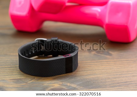wearable device, wirst watch type Sports tracker and pink colored dumb-bell on a wooden board