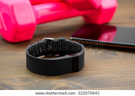 wearable device, wirst watch type Sports tracker with smartphone and pink colored dumb-bell on a wooden board