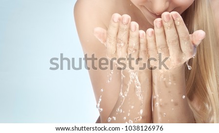 Young beautiful woman cleaning her face with water, morning freshness, removing makeup, skin care health and beauty treatment concept, isolated on blue background
