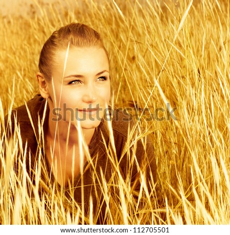 Picture of pretty woman sitting on wheat field, closeup portrait of cute young lady on golden ryes background, autumn harvest concept, happy beautiful girl enjoying cereal meadow, fall season