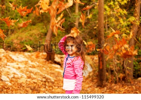 Photo of sweet little girl in autumn forest, adorable child playing game in fall park, pretty kid enjoying autumnal nature, beautiful golden trees foliage, nice warm sunny day