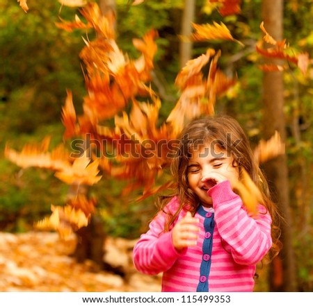 Image of small cute female child enjoying autumn nature, little pretty girl playing game in fall park, beautiful golden trees foliage, nice warm sunny day, carefree childhood
