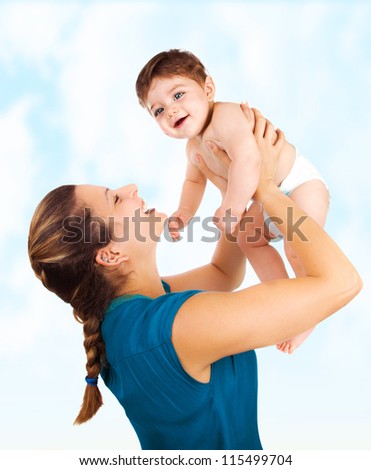 Photo of young beautiful mother with cute baby boy, smiling mommy lift her adorable son, pretty woman throwing up cheerful little child on blue sky background, happy healthy family, love concept