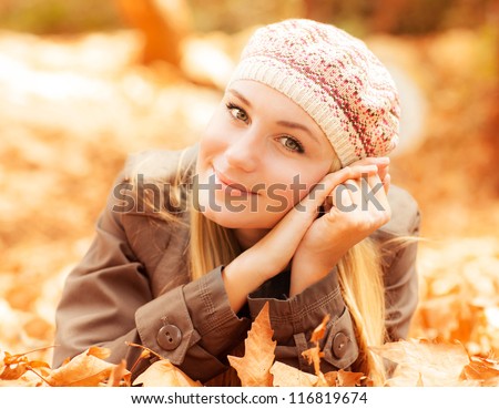 Photo of cute girl laying down on the ground covered dry autumnal foliage in beautiful park in sunny day