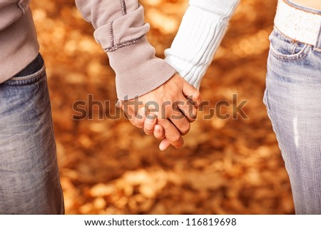 Photo of two loving people holding each other by hands on golden autumnal background