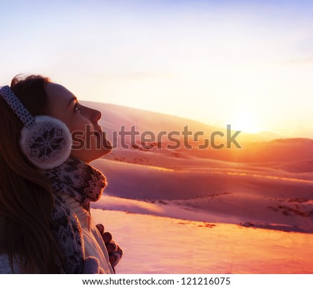 Photo of pretty woman walking in snowy mountains, side view of cute girl looking up, closeup portrait of female wearing warm winter earmuff, red sunset, wintertime sports, trekking and hiking concept