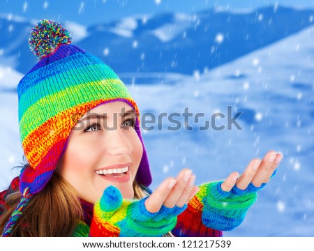 Picture of happy young woman catching snowflakes by hands, cheerful beautiful girl having fun in snowy mountains, attractive female wearing colorful wool hat and gloves, wintertime fashion, Christmas