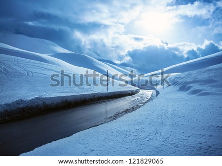 Picture of beautiful snowy highway, black clean asphalt road in mountains covered white snow, wintertime weather, blue cloudy sky, cold frosty day, Christmas vacation, landscape of driveway