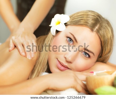 Photo of pretty woman enjoying day spa, cute female lying down on massage table, frangipani flower in hair, alternative treatment, natural cosmetics, luxury spa salon, health care and beauty concept