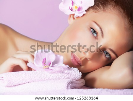 Picture of cute female with pink orchid flower in head lying down on massage table, healthy lifestyle, luxury spa resort, enjoying dayspa, aroma therapy, pampering and skin care concept