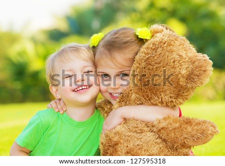 Photo two cute child hugging outdoors, brother and sister having fun on backyard in spring, nice little girl with adorable boy playing with big soft bear toy, best friends, happy childhood concept