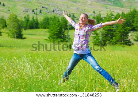 Happy girl jumping on the field, enjoying fresh air and spring green grass, freedom and happiness concept
