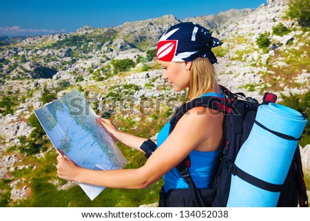 Pretty traveler woman standing in mountains searching right direction in the map, exploration and journey concept