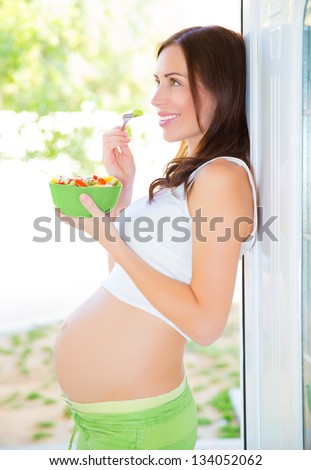 Side view of beautiful pregnant woman eating fresh vegetables salad, happy motherhood, new life concept