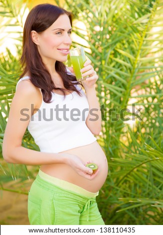 Cute pregnant girl drink fresh kiwi juice outdoor in spring time, healthy lifestyle, having breakfast on backyard, happy motherhood concept