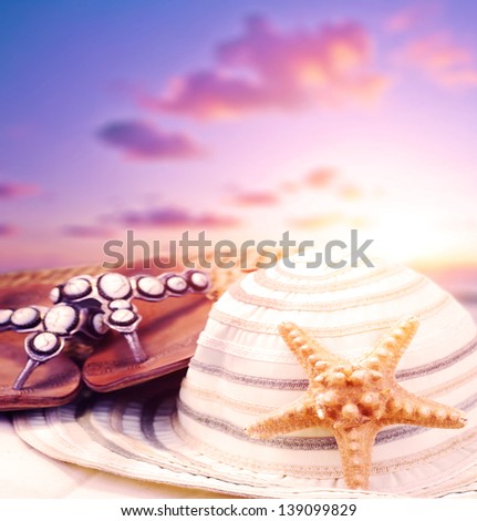 Closeup still life of beach accessories on purple sunset background, flip flops and women\'s hat decorated with starfish, summer holiday and vacation concept