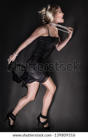 Beautiful angry woman running, wearing sexy black dress and luxury pearl beads, blond fashion model full body length, heartbroken female with mad facial expression, glamorous lady very upset