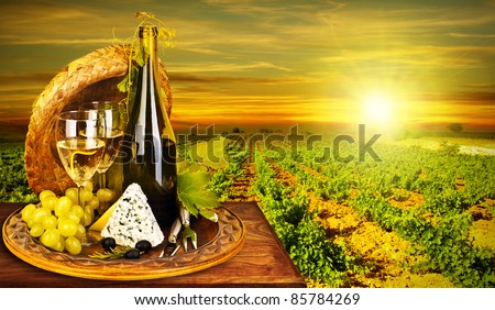 Wine and cheese romantic dinner outdoor, table for two with vineyard view, fresh grapes and wineglass at restaurant, warm autumn sunset, grape field landscape at harvest, food still life