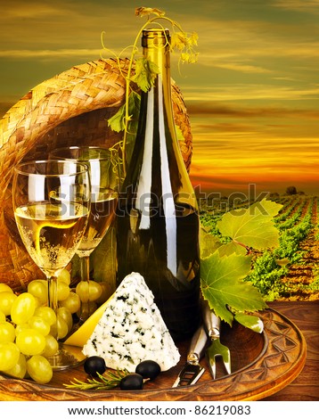 Wine and cheese romantic dinner outdoor, table for two with vineyard view, fresh grapes and wineglass at restaurant, warm autumn sunset, grape field landscape at harvest, food still life