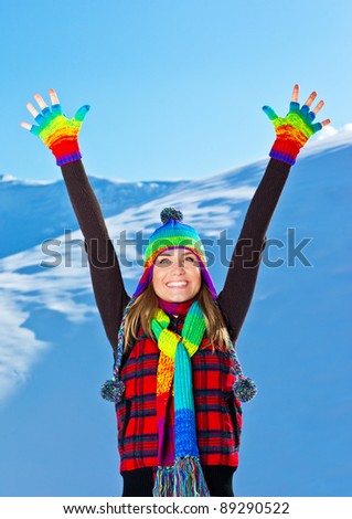 Happy cute girl playing in snow outdoor,looking up with hands up, beautiful woman with raised arms to blue sky & nature,young teen female wearing colorful hat Christmas winter holidays travel vacation