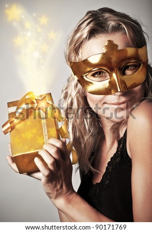 Stylish woman wearing golden mask and holding gift box, celebrating holidays, female receive gold Christmas present, new year eve party