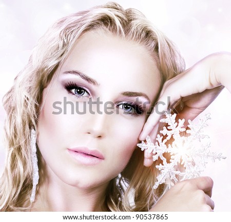 Beautiful woman in Christmas winter style, holding shining snowflake star, glamor female face with bright makeup, sexy girl portrait over abstract pink glowing bokeh holiday background