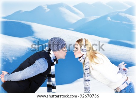 Happy couple kissing, side view face portrait, outdoor at winter snowy mountains, people over natural blue wintertime landscape background, Christmas vacation holidays, love concept
