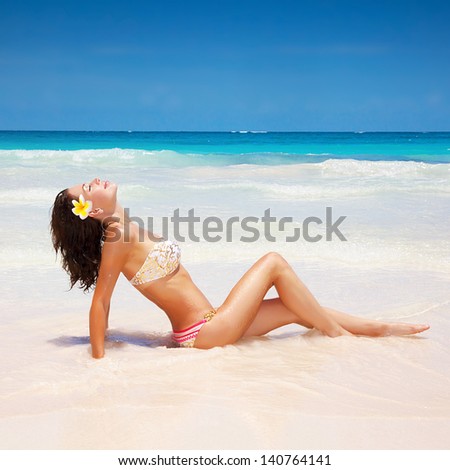 Sexual brunette girl take sunbath on the beach, happy female with frangipani flower in hair wearing stylish colorful swimwear, enjoying summer holidays