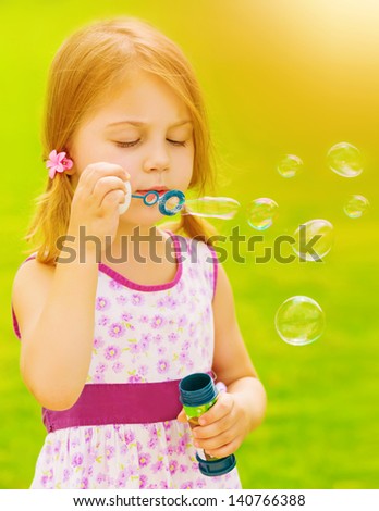 Closeup portrait of cute baby girl blowing soap bubbles outdoors, playing game on spring garden, sunny day, happy childhood concept