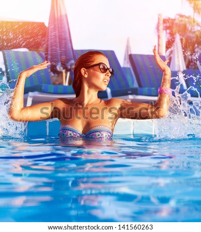Beautiful woman having fun in the pool, making water splash by hands, enjoying hot summer day in swimming-pool, summertime holiday and vacation, refreshment concept
