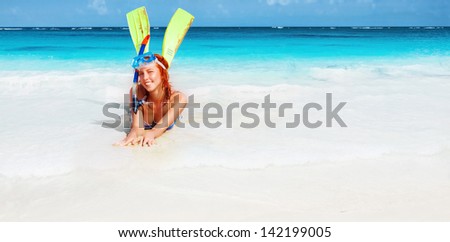 Happy diver girl lying down on beautiful sandy beach, wearing diving mask, tube and fins, active lifestyle, summer holidays, snorkeling concept