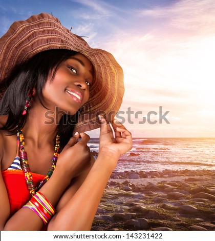 Closeup portrait of beautiful african woman on the beach, sexy model posing on seashore on sunset, wearing stylish hat and fashionable accessories, summer vacation