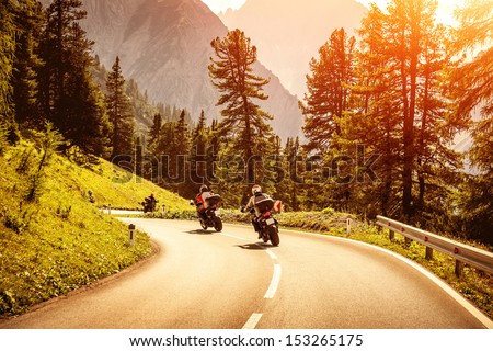 Group Of Motorcyclists Riding On Curves Mountainous Road, Race Of Motorbike In Alps, Beautiful Pine Forest, Red Sunset Light, Extreme Sport Concept